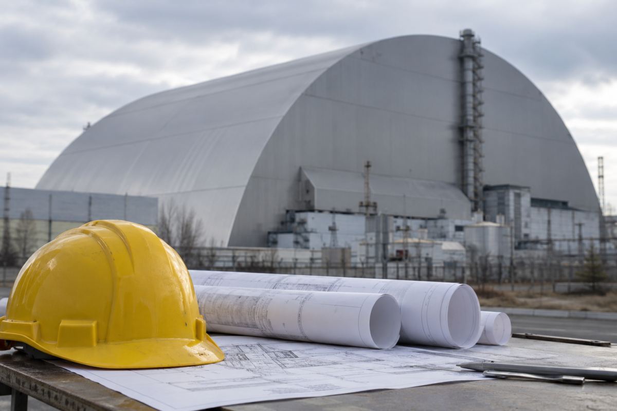 An engineer’s hard hat and plans in front of Chernobyl’s protective confinement.