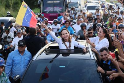 María Corina Machado waves from a vehicle to supporters carrying Venezuelan flags